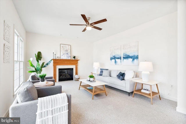 living area featuring baseboards, carpet floors, a glass covered fireplace, and a ceiling fan