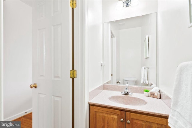 half bathroom with toilet, vanity, and wood finished floors