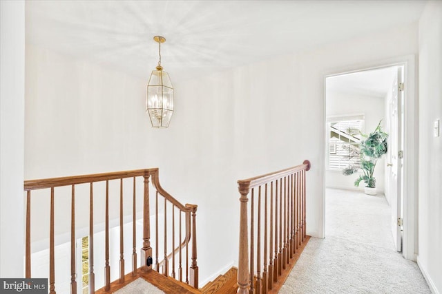 hallway featuring carpet, an upstairs landing, baseboards, and a chandelier