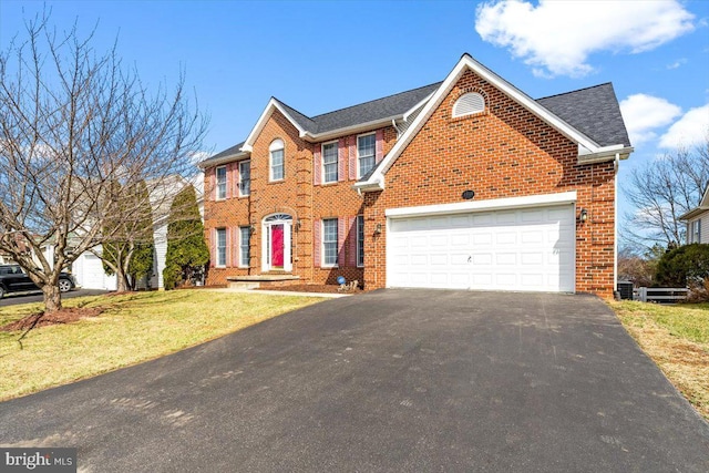 colonial home with brick siding, an attached garage, aphalt driveway, and a front yard