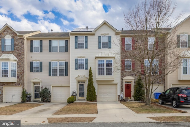 multi unit property with an attached garage, roof mounted solar panels, and driveway