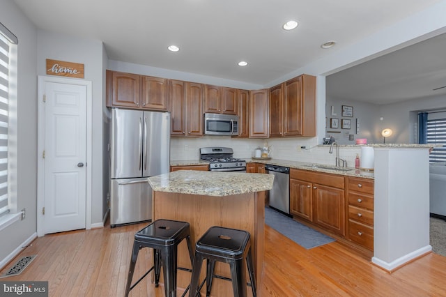 kitchen featuring a breakfast bar area, visible vents, light wood finished floors, decorative backsplash, and appliances with stainless steel finishes