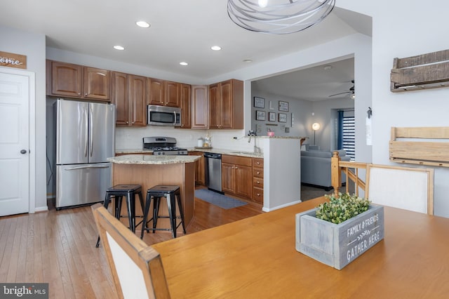 kitchen with light wood finished floors, a kitchen island, a sink, appliances with stainless steel finishes, and backsplash