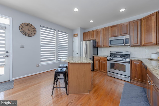 kitchen with decorative backsplash, appliances with stainless steel finishes, a kitchen island, and light wood-style floors