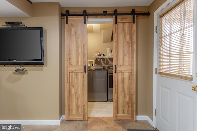 interior space featuring a barn door, separate washer and dryer, light tile patterned floors, baseboards, and laundry area