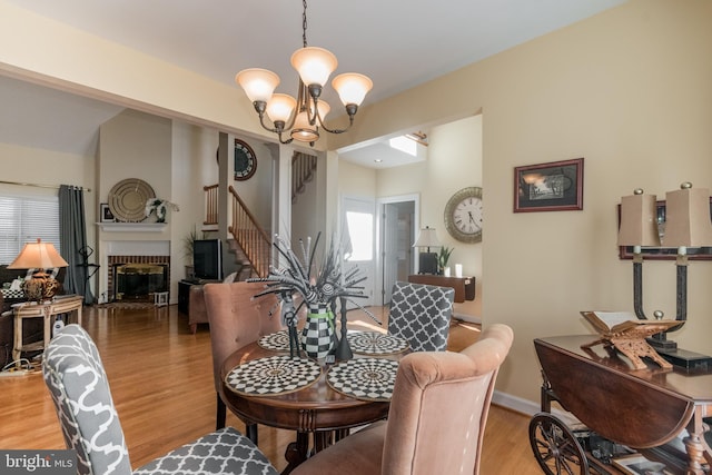 dining area featuring a brick fireplace, baseboards, stairway, light wood-type flooring, and a notable chandelier