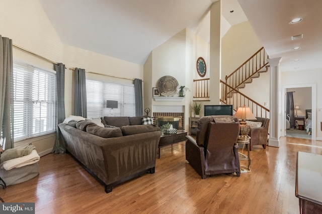 living room featuring visible vents, high vaulted ceiling, light wood-style floors, a fireplace, and stairs