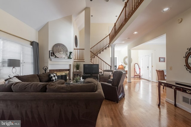 living area with stairway, wood finished floors, a high ceiling, and a fireplace