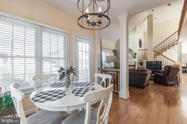 dining area with a glass covered fireplace, decorative columns, an inviting chandelier, and wood finished floors