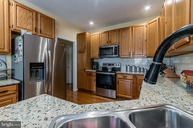 kitchen with light stone countertops, backsplash, appliances with stainless steel finishes, and brown cabinetry