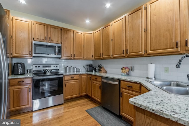 kitchen with light wood-type flooring, a sink, tasteful backsplash, stainless steel appliances, and light stone countertops