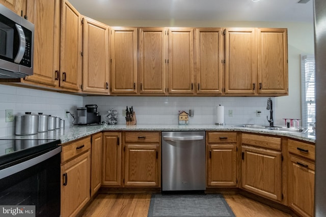 kitchen featuring tasteful backsplash, light stone counters, light wood-style flooring, stainless steel appliances, and a sink