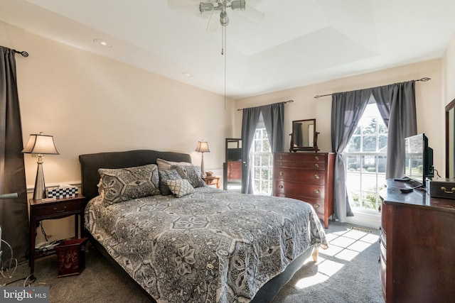 carpeted bedroom with a raised ceiling and ceiling fan