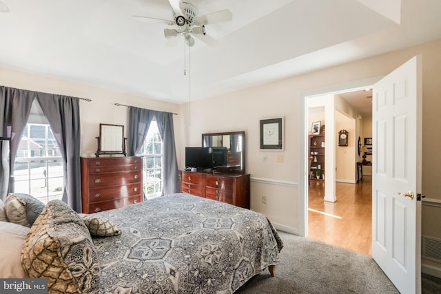 bedroom featuring a ceiling fan, a tray ceiling, wood finished floors, and baseboards