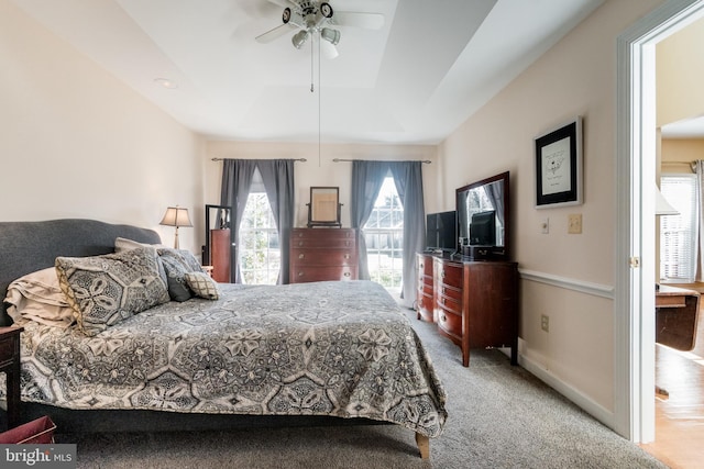 carpeted bedroom featuring a raised ceiling, a ceiling fan, and baseboards