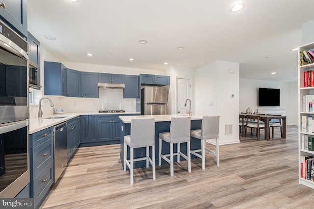 kitchen with light wood finished floors, stainless steel appliances, light countertops, a sink, and under cabinet range hood