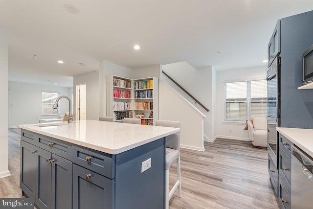 kitchen featuring dishwasher, a breakfast bar, light countertops, light wood-type flooring, and a sink