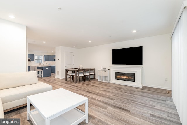 living room featuring baseboards, light wood finished floors, a glass covered fireplace, and recessed lighting