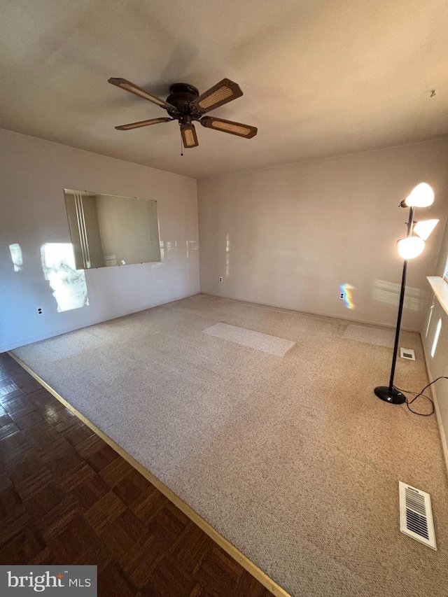 spare room featuring a ceiling fan, dark colored carpet, and visible vents