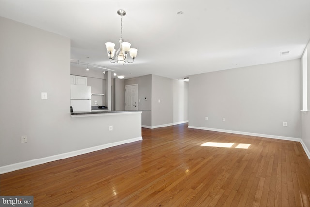 unfurnished living room with wood-type flooring, track lighting, a chandelier, and baseboards