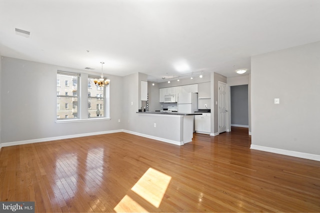 unfurnished living room featuring rail lighting, visible vents, an inviting chandelier, baseboards, and hardwood / wood-style flooring