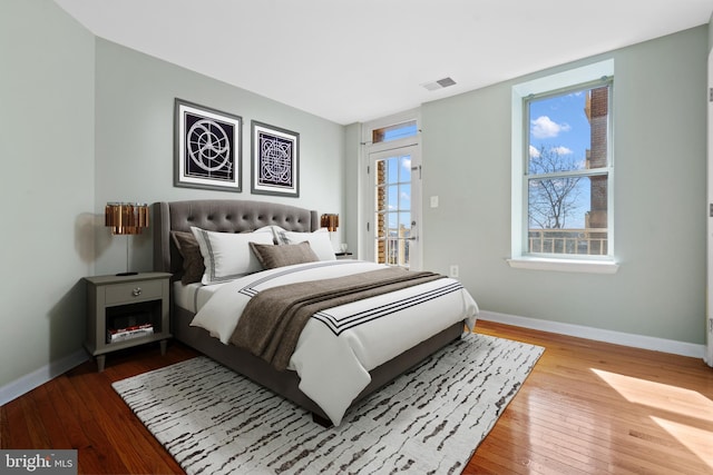 bedroom featuring access to outside, wood-type flooring, visible vents, and baseboards