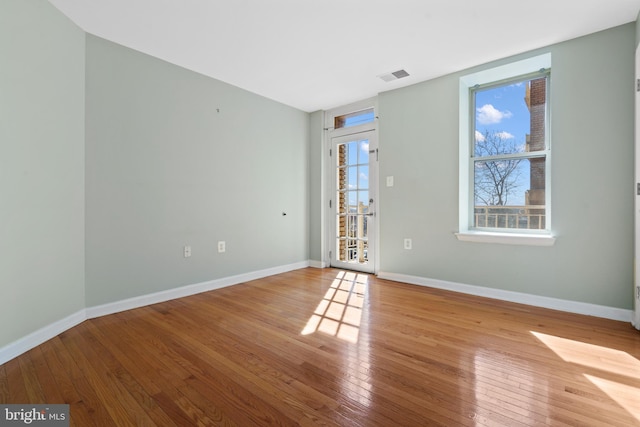 unfurnished room with wood-type flooring, visible vents, and baseboards