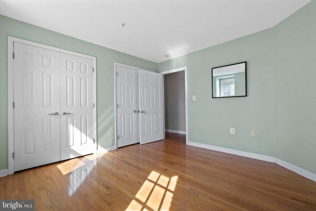 unfurnished bedroom featuring hardwood / wood-style flooring, baseboards, and two closets