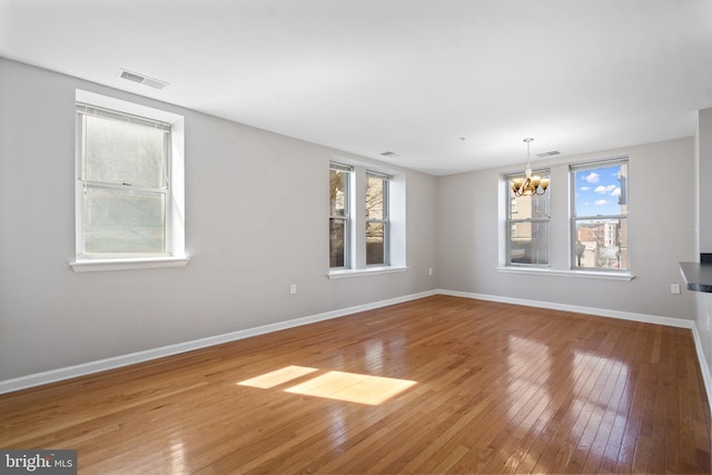 unfurnished room featuring hardwood / wood-style floors, a healthy amount of sunlight, visible vents, and baseboards