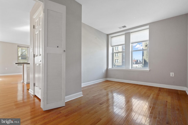 spare room with light wood finished floors, visible vents, and baseboards