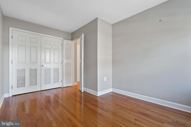 unfurnished bedroom with hardwood / wood-style floors, a closet, and baseboards