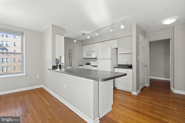 kitchen featuring a peninsula, white appliances, white cabinetry, baseboards, and light wood-style floors