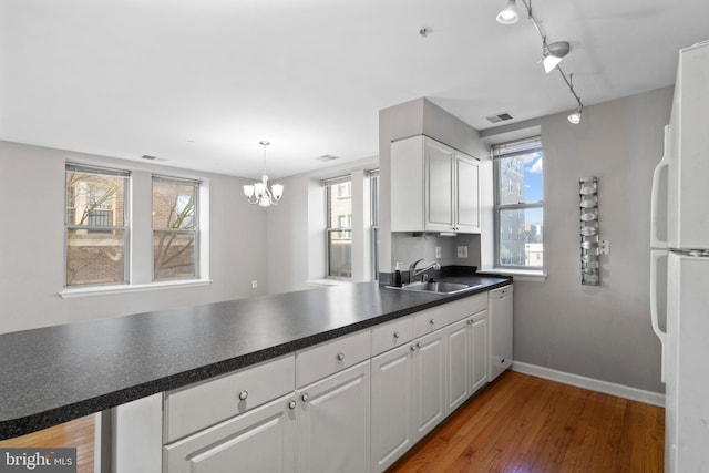 kitchen featuring a peninsula, white appliances, a sink, visible vents, and white cabinets