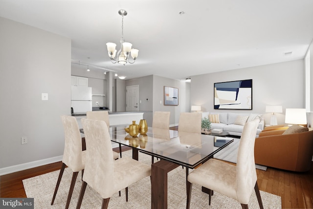 dining area with rail lighting, a notable chandelier, baseboards, and wood finished floors