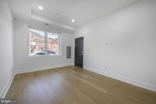 empty room featuring electric panel, visible vents, baseboards, wood finished floors, and recessed lighting