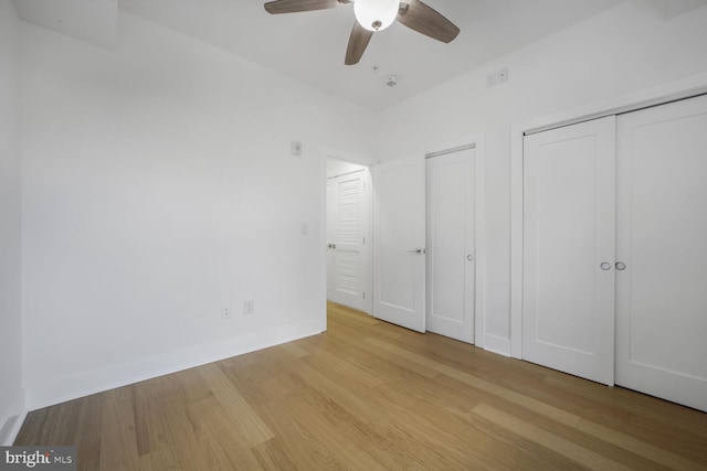 unfurnished bedroom featuring ceiling fan, two closets, baseboards, and wood finished floors