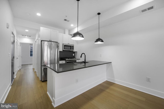 kitchen featuring dark countertops, visible vents, appliances with stainless steel finishes, a sink, and wood finished floors