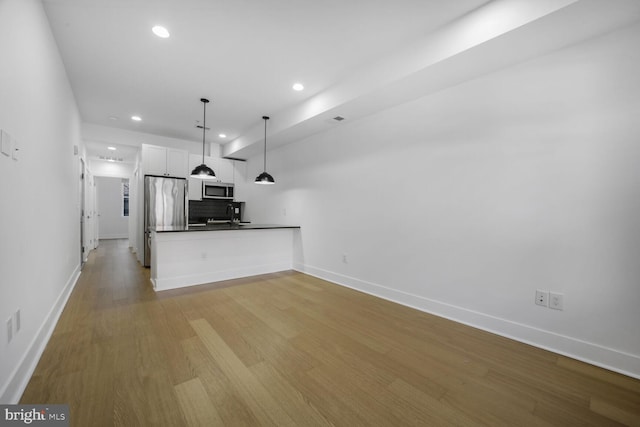 kitchen with light wood-style flooring, stainless steel appliances, a sink, white cabinets, and dark countertops