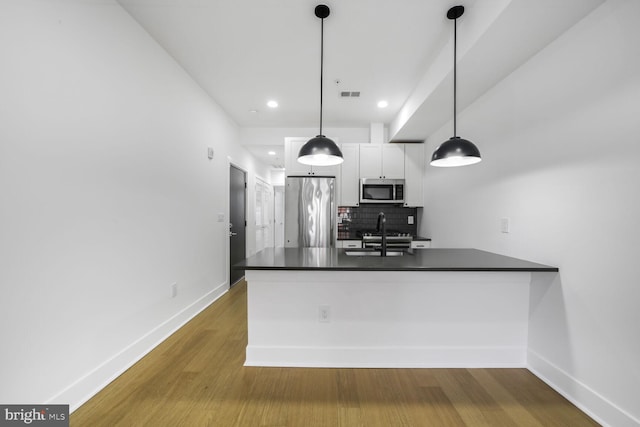 kitchen featuring decorative backsplash, dark countertops, stainless steel appliances, white cabinetry, and a sink