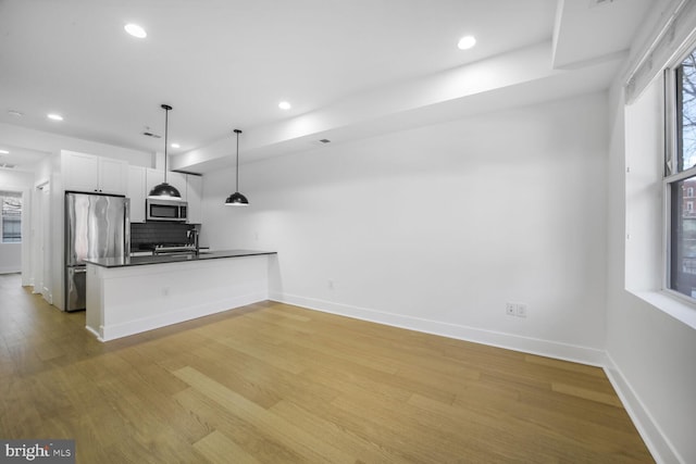 kitchen featuring stainless steel appliances, baseboards, light wood-type flooring, backsplash, and dark countertops