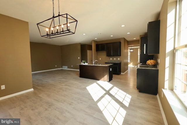 kitchen with a notable chandelier, open floor plan, a sink, an island with sink, and baseboards