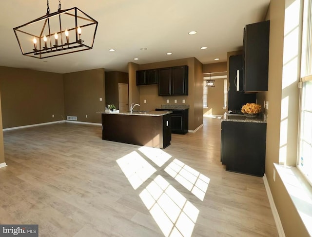 kitchen with a sink, baseboards, open floor plan, light wood finished floors, and an island with sink