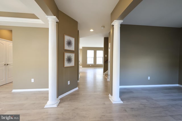 interior space featuring baseboards, light wood-style floors, and ornate columns