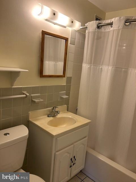 bathroom featuring toilet, vanity, tile walls, tile patterned floors, and shower / bath combo