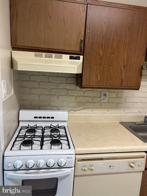 kitchen with under cabinet range hood, white appliances, a sink, light countertops, and backsplash