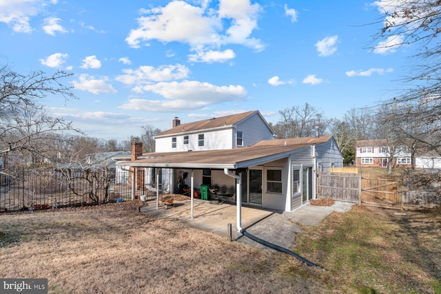 rear view of house featuring a patio, a chimney, a sunroom, a gate, and fence private yard