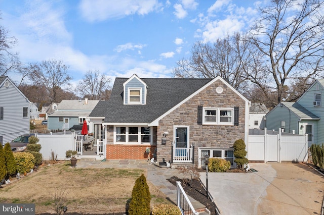 view of front facade featuring a shingled roof, a gate, fence, and stone siding