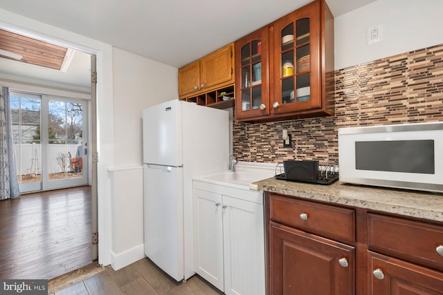 kitchen with light stone counters, backsplash, glass insert cabinets, light wood-type flooring, and white appliances