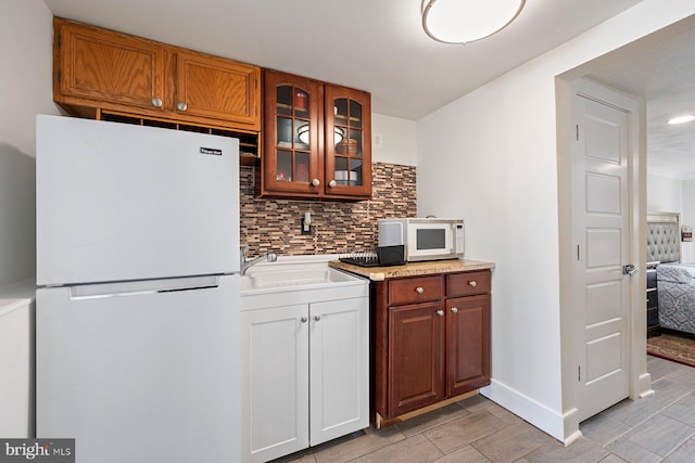 kitchen with white appliances, glass insert cabinets, backsplash, light countertops, and a sink