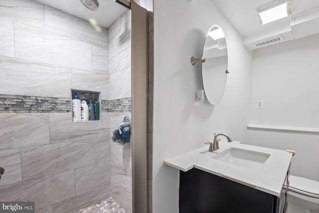 bathroom featuring toilet, a tile shower, and vanity